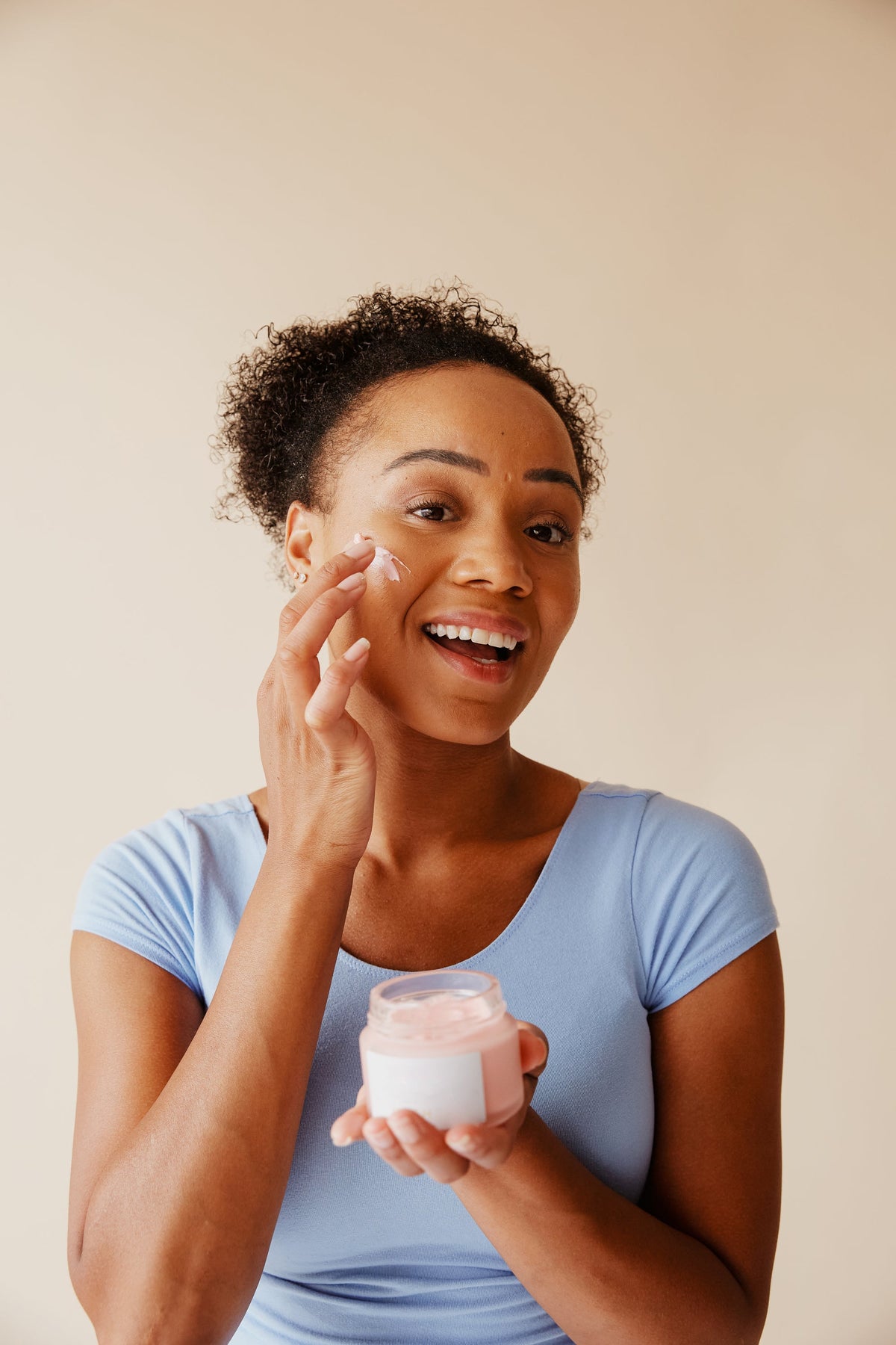 Mujer sonriendo mientras aplica crema facial